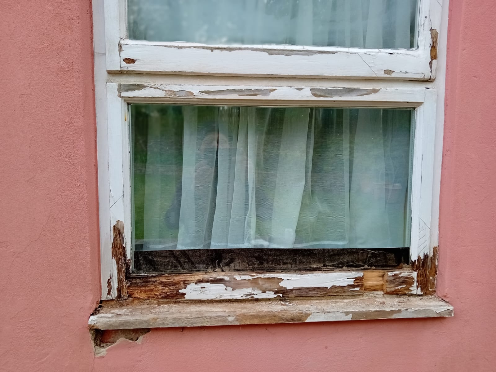 Casement window before restoration — peeling paint and rotten sill on pink wall