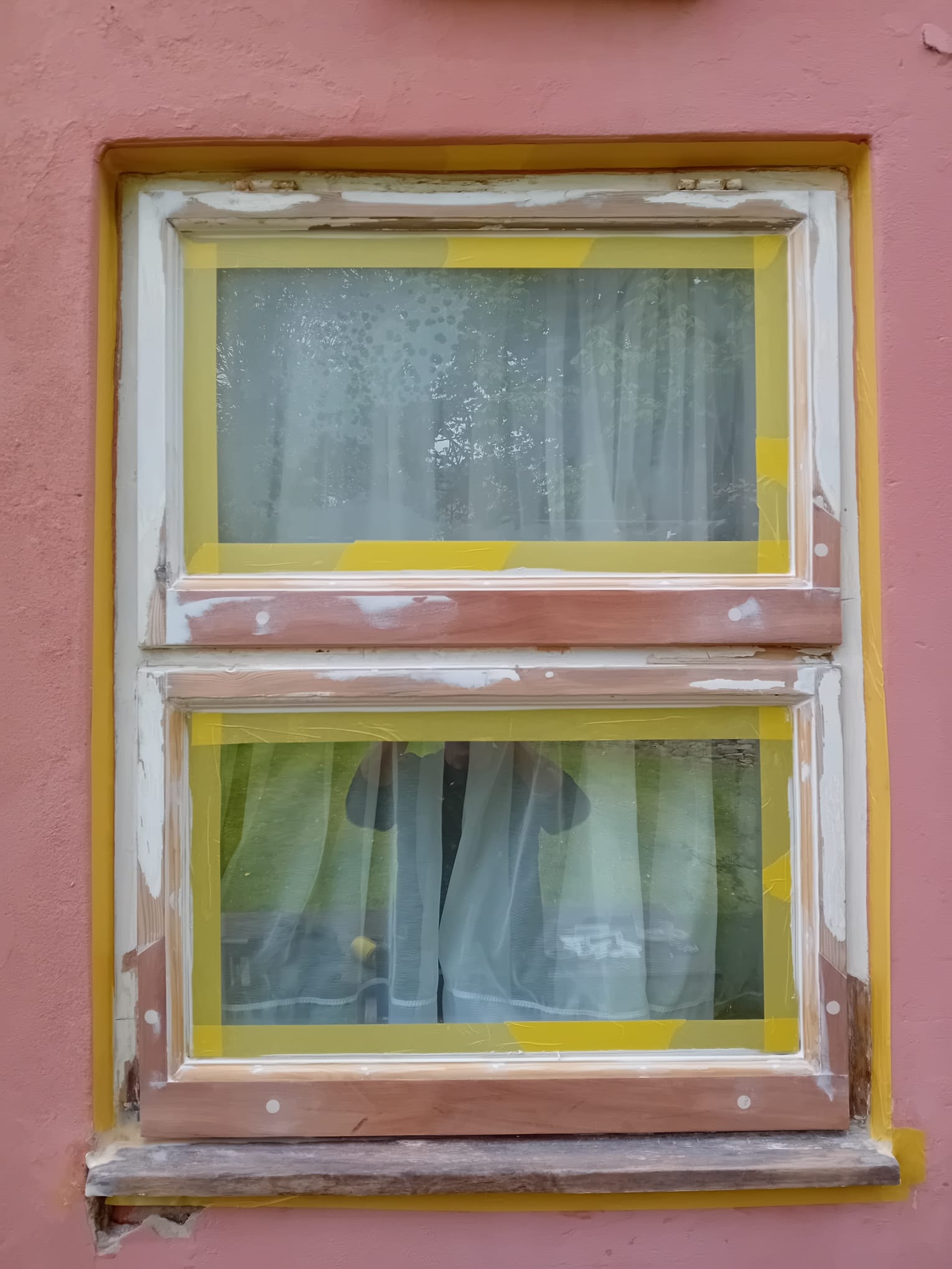 Casement window mid-restoration — primed and masked with yellow tape